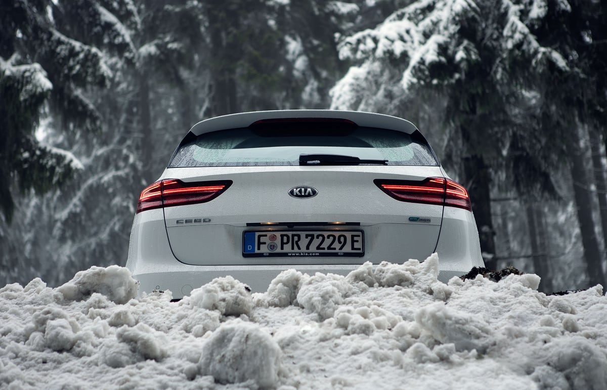 Weißer KIA Ceed im Schnee zwischen verschneiten Tannen