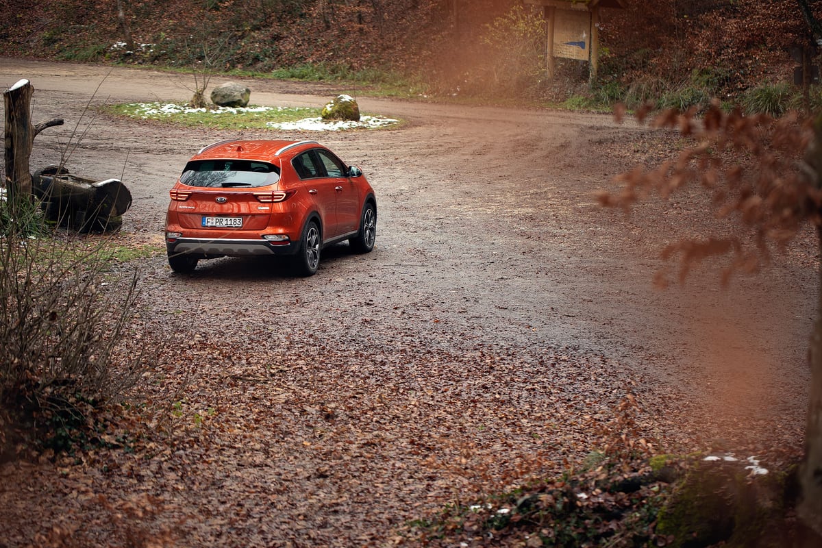 Orangefarbener KIA Sportage auf einem Waldweg im Herbstlaub