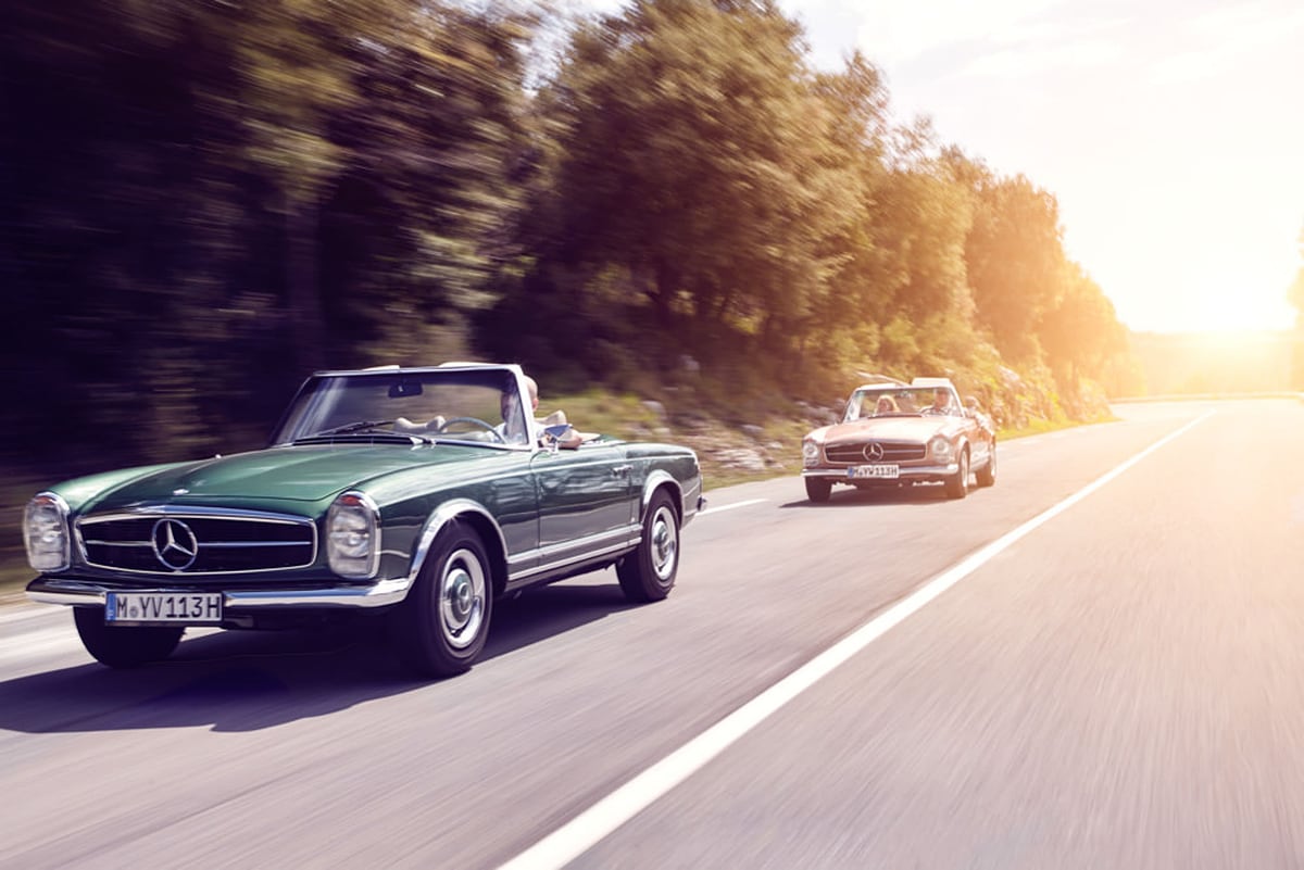 Zwei Mercedes-Benz Oldtimer-Cabrios in Fahrt auf einer Küstenstraße bei Cannes im Gegenlicht