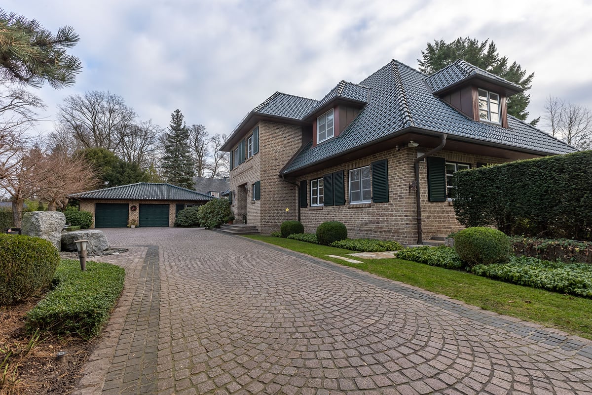 Außenansicht einer Villa mit Auffahrt und großen Bäumen