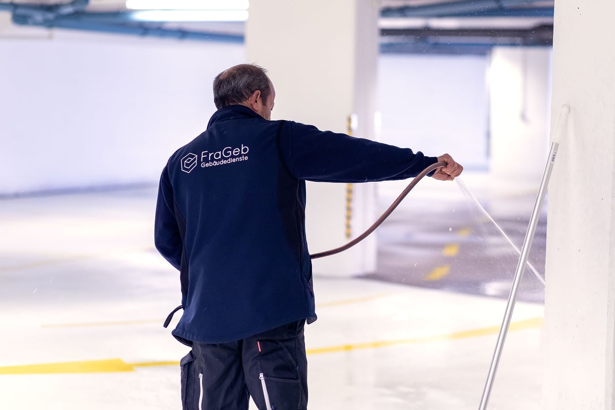 Mitarbeiter eines Gebäudereinigers mit Hochdruckschlauch in einer Tiefgarage