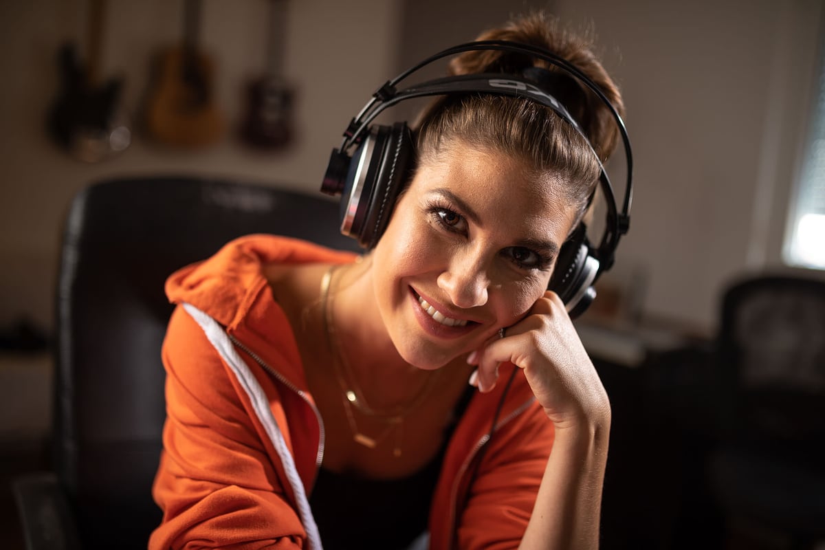 Musikerin mit Kopfhörern lacht am Keyboard im Studio