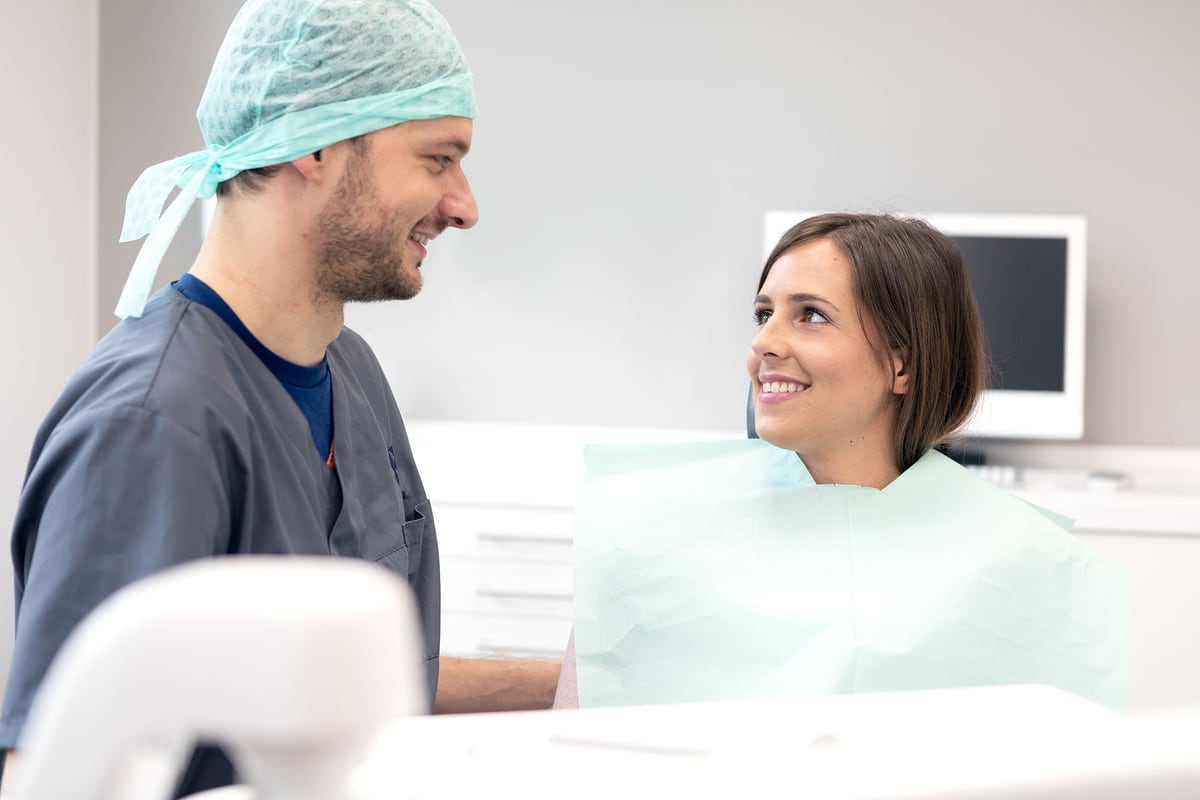Zahnarzt im Gespräch mit einer lächelnden Patientin auf dem Behandlungsstuhl